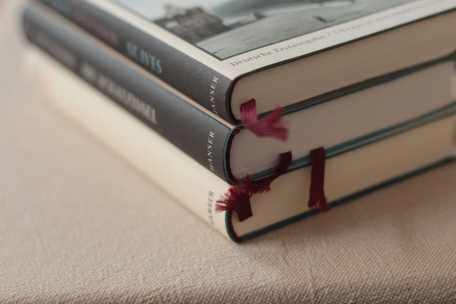 رزمة كتب مجلّدة مكدّسة على طاولة بيج دافئة، تخرج من بينها شرائط فاصلة رفيعة، بضوء نهاريّ ناعم.